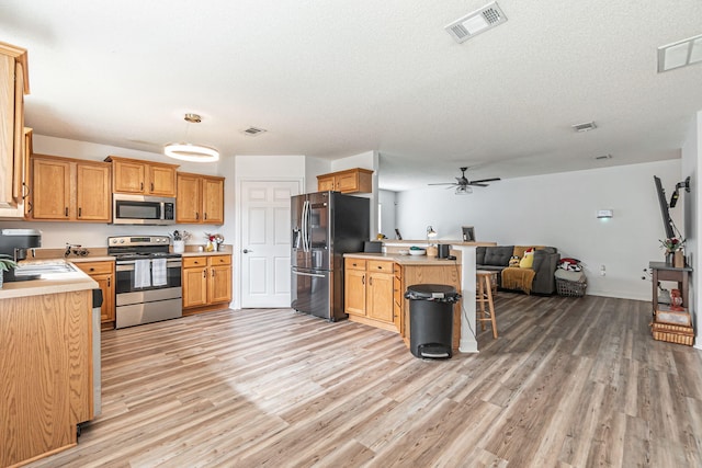 kitchen with a peninsula, visible vents, light wood-style floors, open floor plan, and appliances with stainless steel finishes