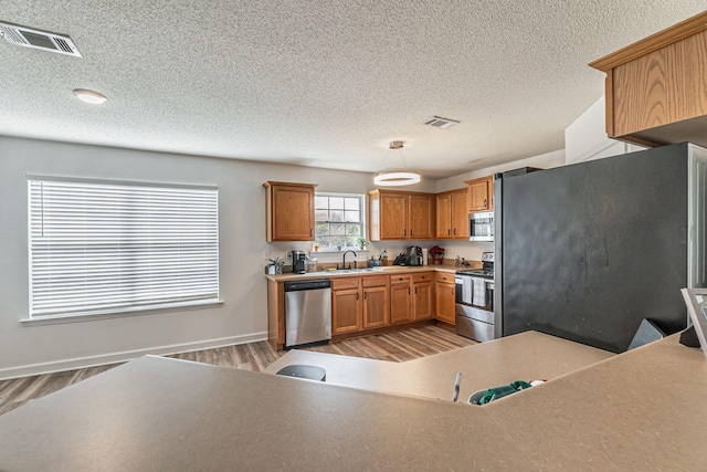 kitchen with light wood finished floors, visible vents, appliances with stainless steel finishes, and brown cabinets