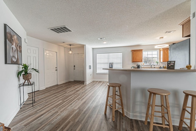 kitchen featuring visible vents, dark wood-style floors, a kitchen breakfast bar, a peninsula, and a sink