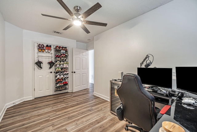 office area with a ceiling fan, visible vents, baseboards, and wood finished floors