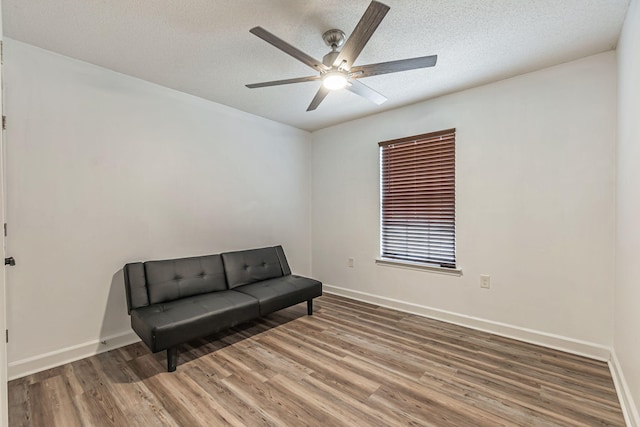 sitting room with ceiling fan, a textured ceiling, baseboards, and wood finished floors