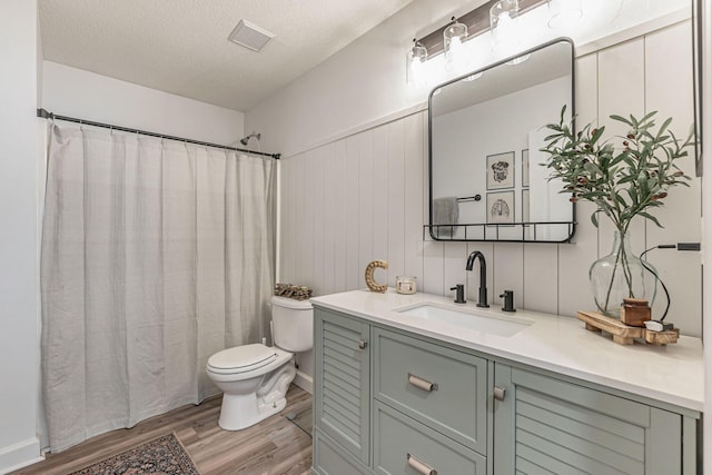 bathroom featuring a textured ceiling, toilet, wood finished floors, vanity, and visible vents