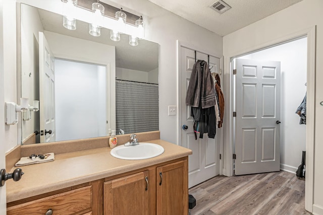 full bathroom with a textured ceiling, visible vents, wood finished floors, and vanity