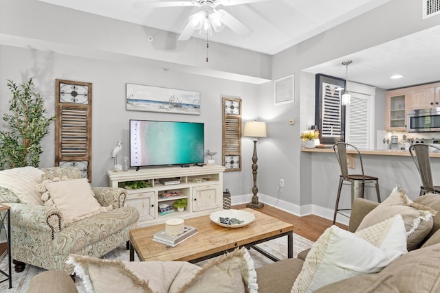 living area with a ceiling fan, wood finished floors, visible vents, and baseboards