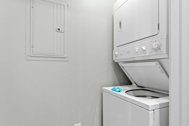 washroom featuring stacked washer / drying machine, laundry area, and electric panel