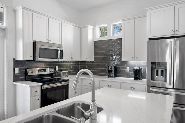 kitchen with tasteful backsplash, white cabinetry, stainless steel appliances, and light stone counters