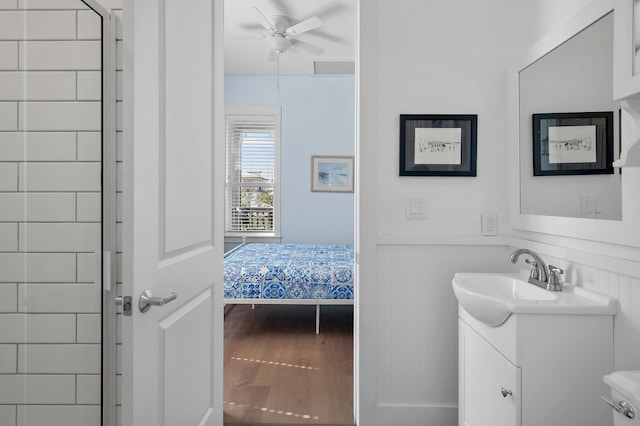 bathroom with a wainscoted wall, a ceiling fan, vanity, wood finished floors, and tiled shower