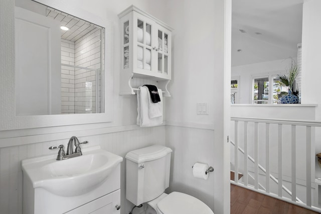 bathroom with toilet, a wainscoted wall, wood finished floors, vanity, and vaulted ceiling