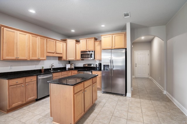 kitchen with arched walkways, stainless steel appliances, visible vents, a sink, and a kitchen island