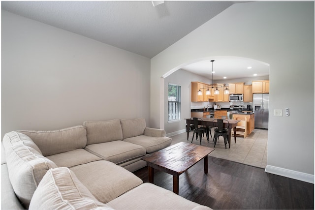 living room with arched walkways, recessed lighting, vaulted ceiling, light wood-type flooring, and baseboards