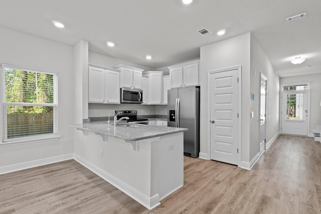 kitchen with a peninsula, visible vents, light wood-style floors, white cabinets, and appliances with stainless steel finishes