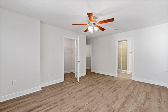 unfurnished bedroom with baseboards, ceiling fan, light wood-style flooring, a walk in closet, and a closet