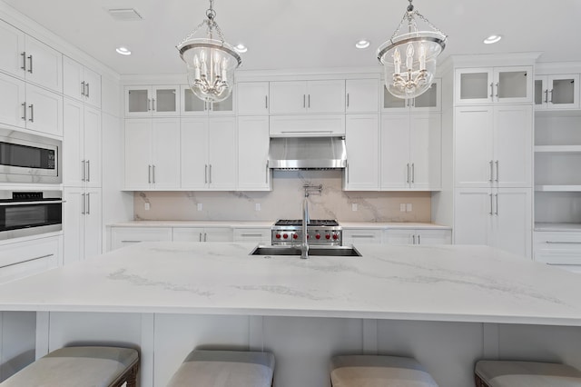 kitchen with a breakfast bar area, stainless steel appliances, a sink, ventilation hood, and an inviting chandelier