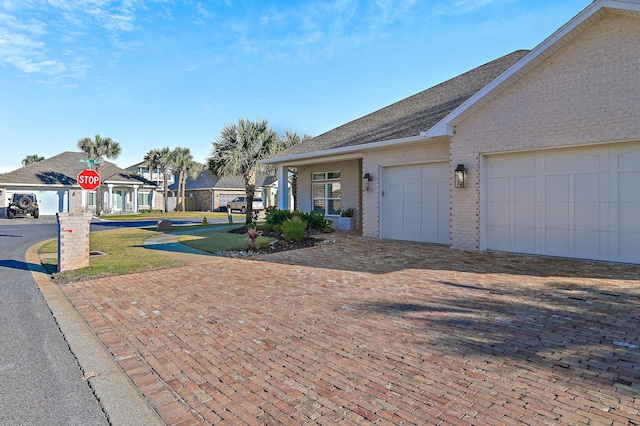 view of front of property featuring roof with shingles, decorative driveway, and brick siding