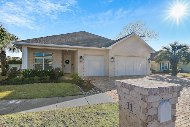 ranch-style home featuring an attached garage, roof with shingles, decorative driveway, and brick siding