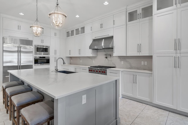 kitchen featuring decorative backsplash, white cabinetry, a sink, built in appliances, and under cabinet range hood