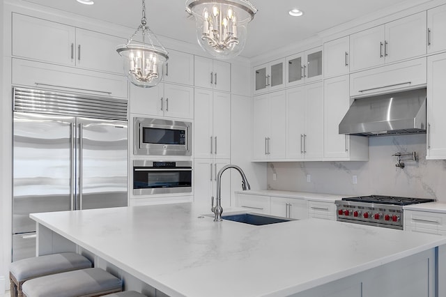 kitchen featuring a breakfast bar area, built in appliances, under cabinet range hood, white cabinetry, and a sink