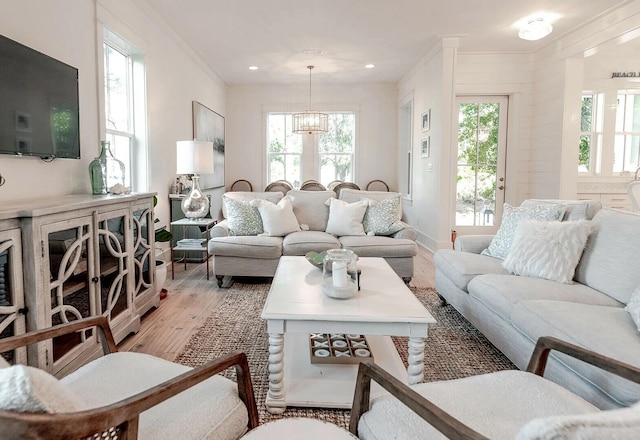 living room featuring light wood-type flooring, a healthy amount of sunlight, ornamental molding, and a chandelier