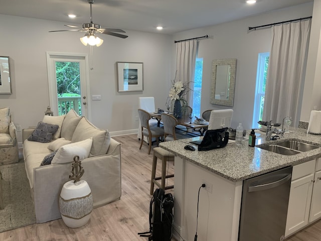 interior space with stainless steel dishwasher, white cabinets, a sink, light stone countertops, and light wood-type flooring