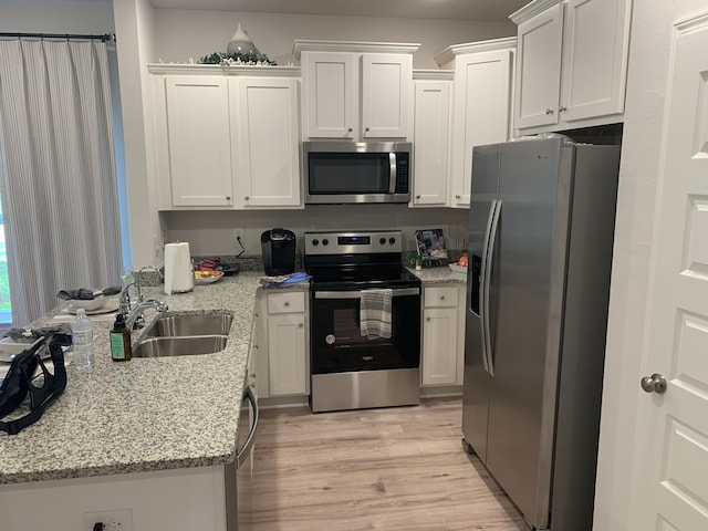 kitchen featuring appliances with stainless steel finishes, white cabinets, a sink, light stone countertops, and light wood-type flooring