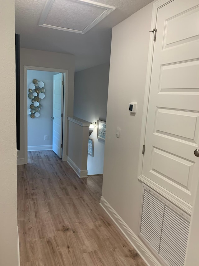 hall featuring wood finished floors, an upstairs landing, baseboards, visible vents, and attic access