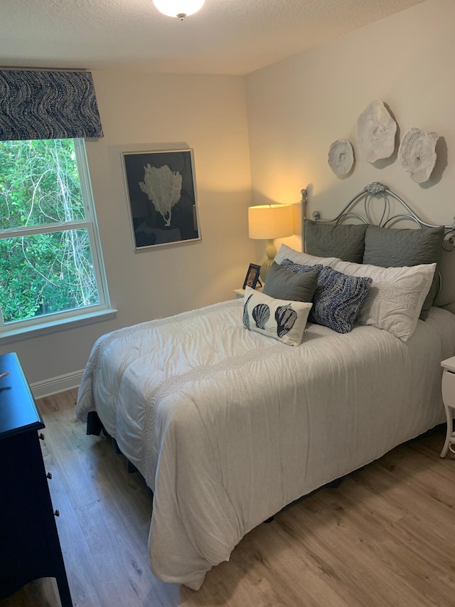 bedroom with a textured ceiling, wood finished floors, and baseboards