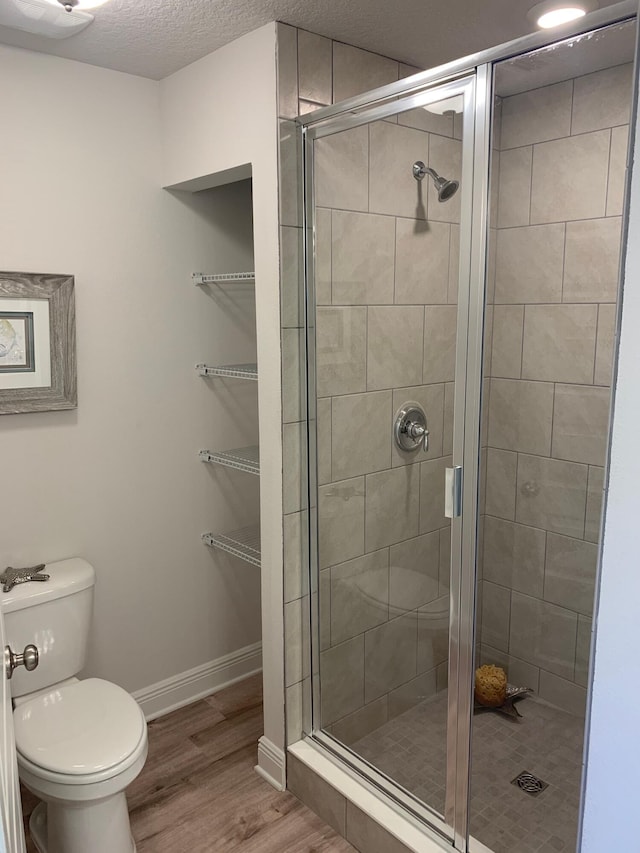 full bathroom with wood finished floors, a shower stall, toilet, and baseboards