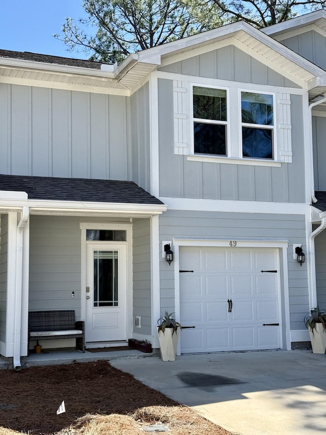 doorway to property featuring a garage, roof with shingles, board and batten siding, and driveway