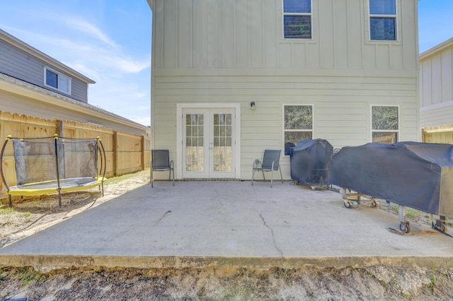 rear view of house featuring fence, french doors, board and batten siding, a trampoline, and a patio area