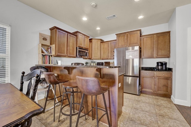 kitchen featuring light tile patterned floors, stainless steel appliances, a breakfast bar area, and brown cabinetry