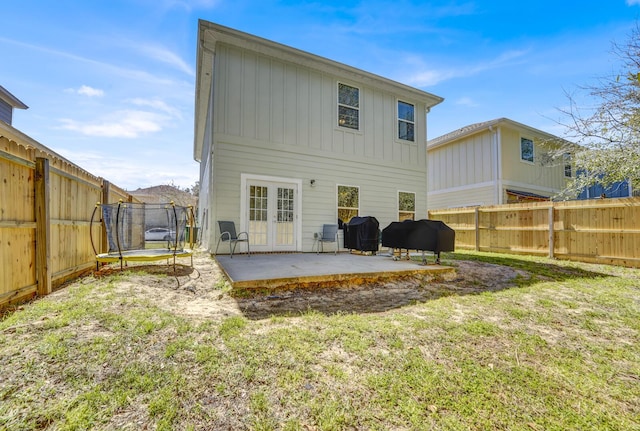 rear view of house with a patio, a fenced backyard, a trampoline, french doors, and board and batten siding