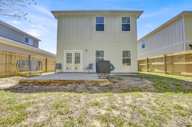 back of house with a patio, a fenced backyard, french doors, board and batten siding, and a trampoline