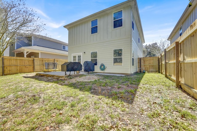 back of property with board and batten siding, a patio area, a fenced backyard, and a lawn