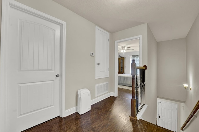 corridor with a textured ceiling, visible vents, an upstairs landing, baseboards, and dark wood-style floors