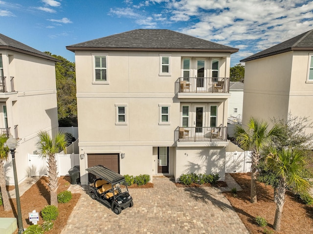 rear view of house featuring a garage, a balcony, fence, decorative driveway, and stucco siding