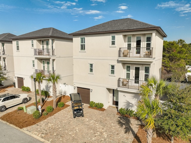 view of front of house featuring a garage, french doors, a balcony, and stucco siding