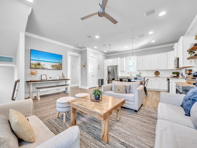 living area featuring recessed lighting, visible vents, baseboards, ornamental molding, and light wood finished floors