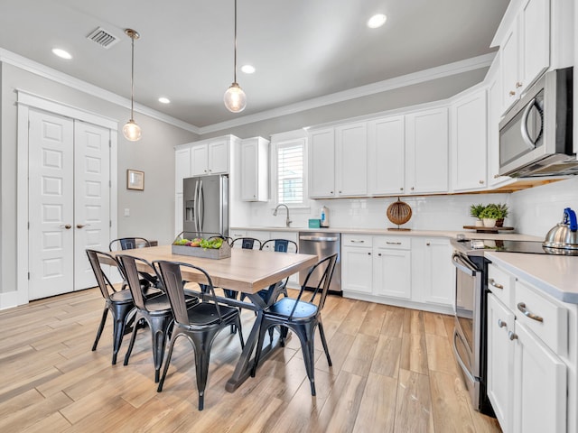 kitchen with crown molding, stainless steel appliances, light countertops, visible vents, and light wood-style flooring