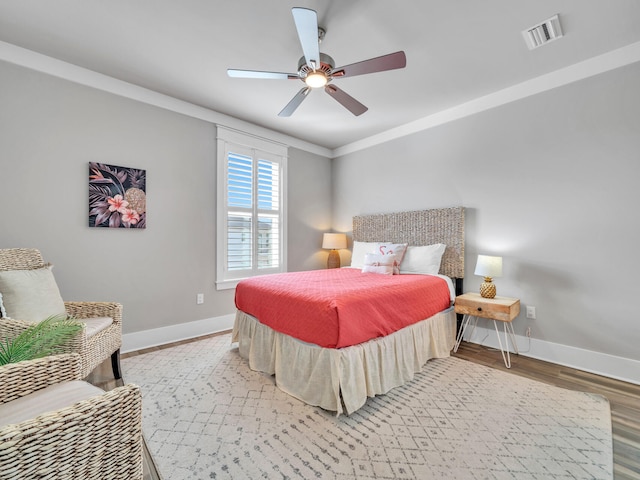 bedroom featuring wood finished floors, a ceiling fan, visible vents, baseboards, and ornamental molding