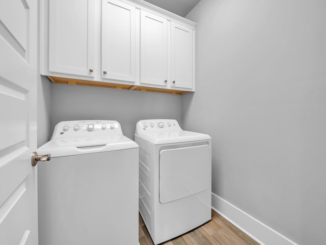 laundry room featuring cabinet space, washing machine and dryer, baseboards, and light wood finished floors