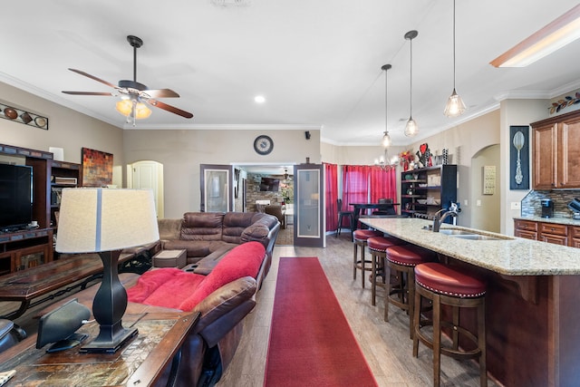 living area with ceiling fan with notable chandelier, arched walkways, crown molding, and wood finished floors