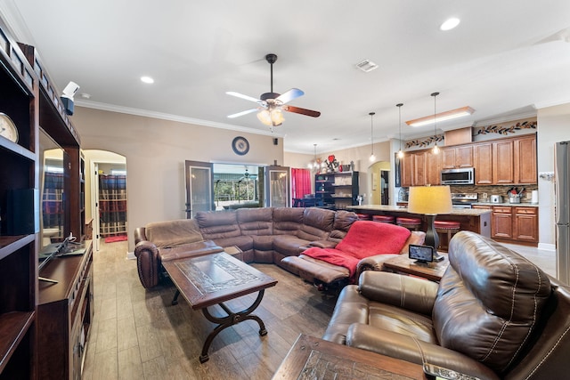 living area featuring arched walkways, visible vents, a ceiling fan, ornamental molding, and light wood-type flooring