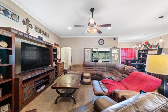 living area featuring ornamental molding, arched walkways, ceiling fan with notable chandelier, and wood finished floors