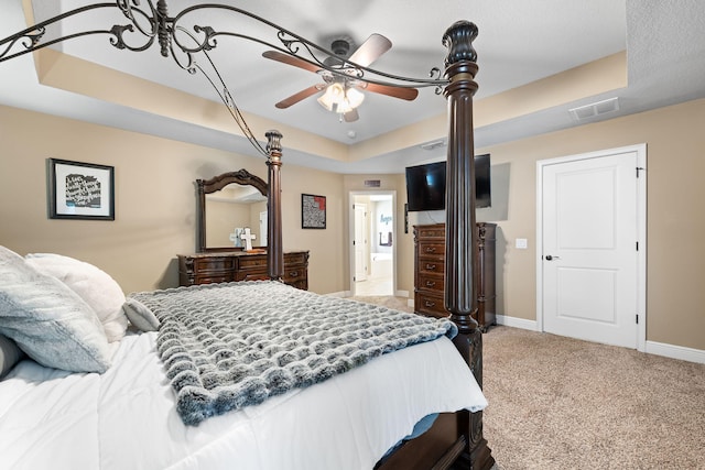 bedroom with a tray ceiling, light colored carpet, visible vents, ceiling fan, and baseboards