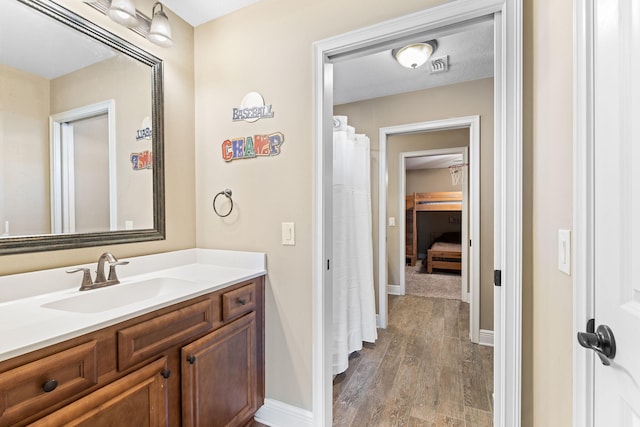 bathroom with visible vents, vanity, baseboards, and wood finished floors