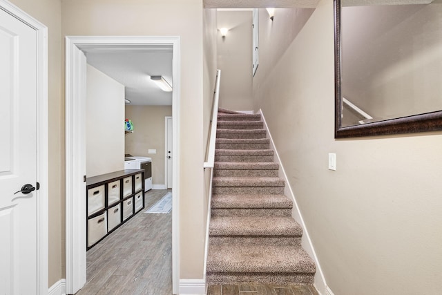 staircase with wood finished floors, washer / dryer, and baseboards