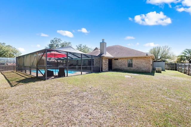 back of house featuring glass enclosure, brick siding, a lawn, and a fenced backyard