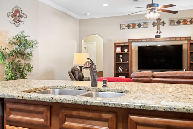 kitchen with ceiling fan, arched walkways, a sink, light stone countertops, and crown molding