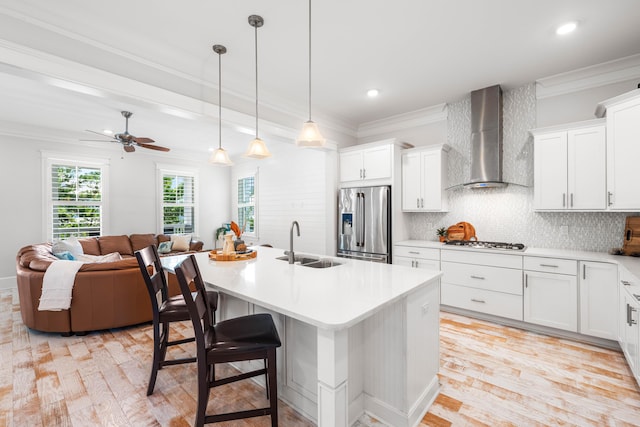 kitchen with a sink, ornamental molding, wall chimney range hood, appliances with stainless steel finishes, and backsplash