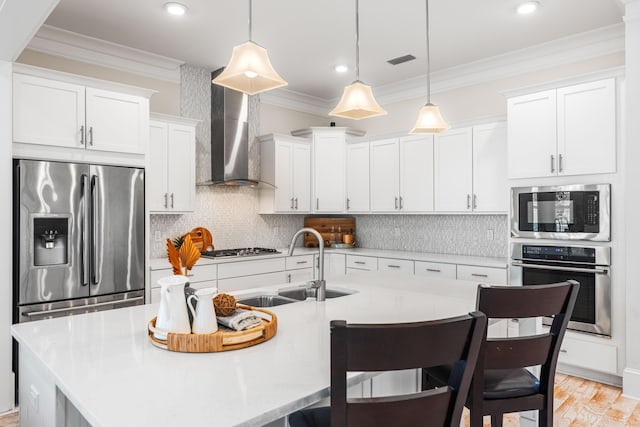 kitchen featuring wall chimney exhaust hood, appliances with stainless steel finishes, a kitchen breakfast bar, ornamental molding, and a sink